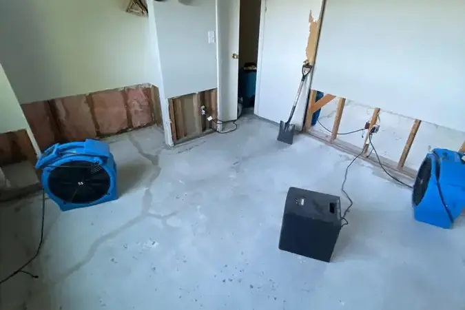 Air movers and a dehumidifier running in a Lewisburg home where the lower drywall has been cut away to a bare floor.