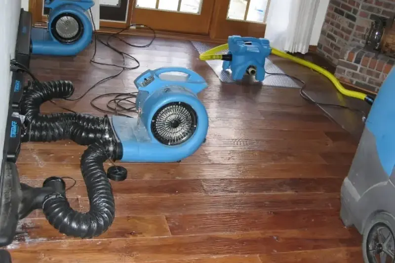 Air movers and lay-flat ducting on a hardwood floor beside a brick fireplace while a Columbia, Tennessee home dries after water damage.