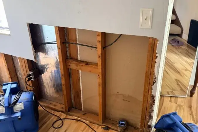 Air movers running beside a wall opened at the bottom during water damage drying in a Fairview, TN home